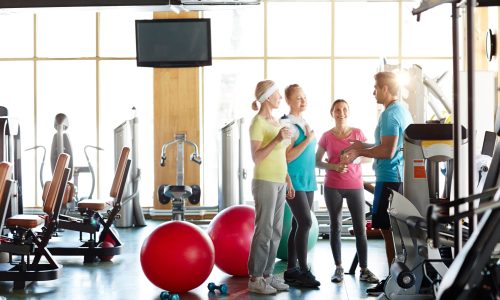 Young fitness coach having talk to group of trainees during break after first part of training