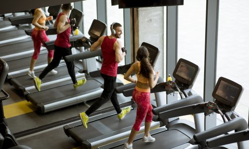 Man and woman doing cardio workout on treadmills in fitness club