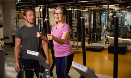 Male trainer looking at mature caucasian woman wearing sportswear running on treadmill in gym. Concept of modern healthy lifestyle