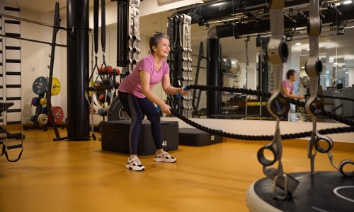 Mature smiling european woman wearing sportswear doing sport exercise with ropes in gym. Concept of modern healthy lifestyle