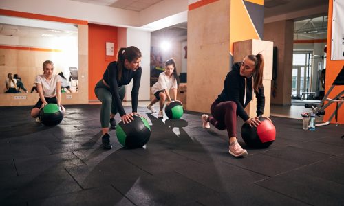 Group of young motivated women exercising on gym floor and using big fitness balls