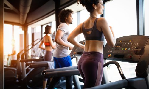 Young fit people running on a treadmill in health club.