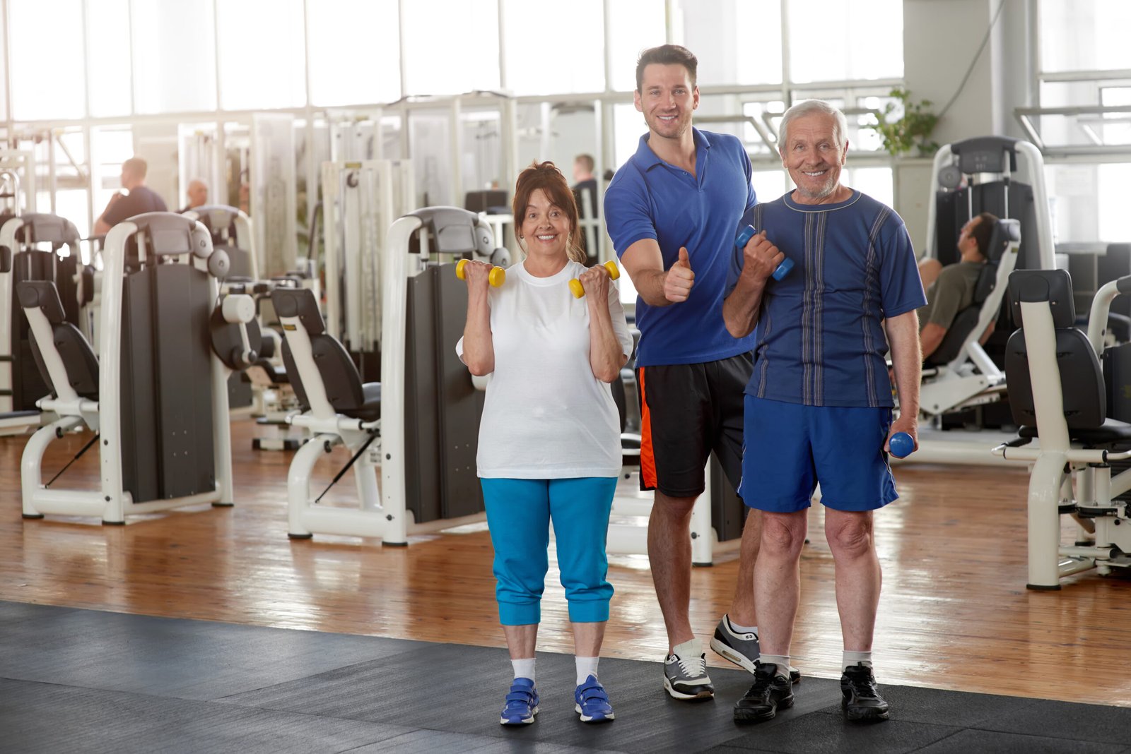 Senior people with trainer at fitness club. Happy smiling elderly couple and and personal trainer showing thumb up after wokrout. Sport, fitness, lifestyle, gesture and people concept.