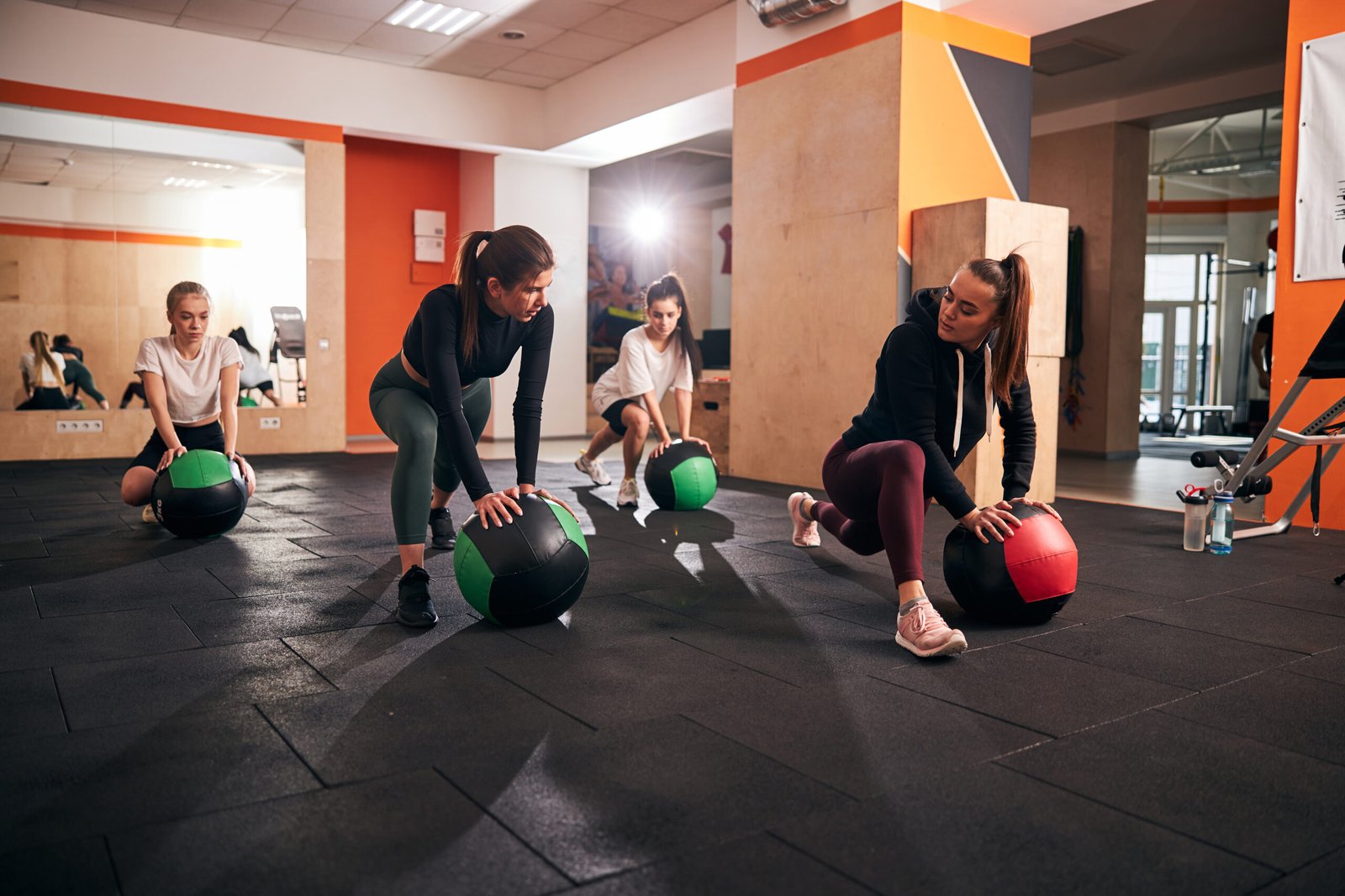 Group of young motivated women exercising on gym floor and using big fitness balls