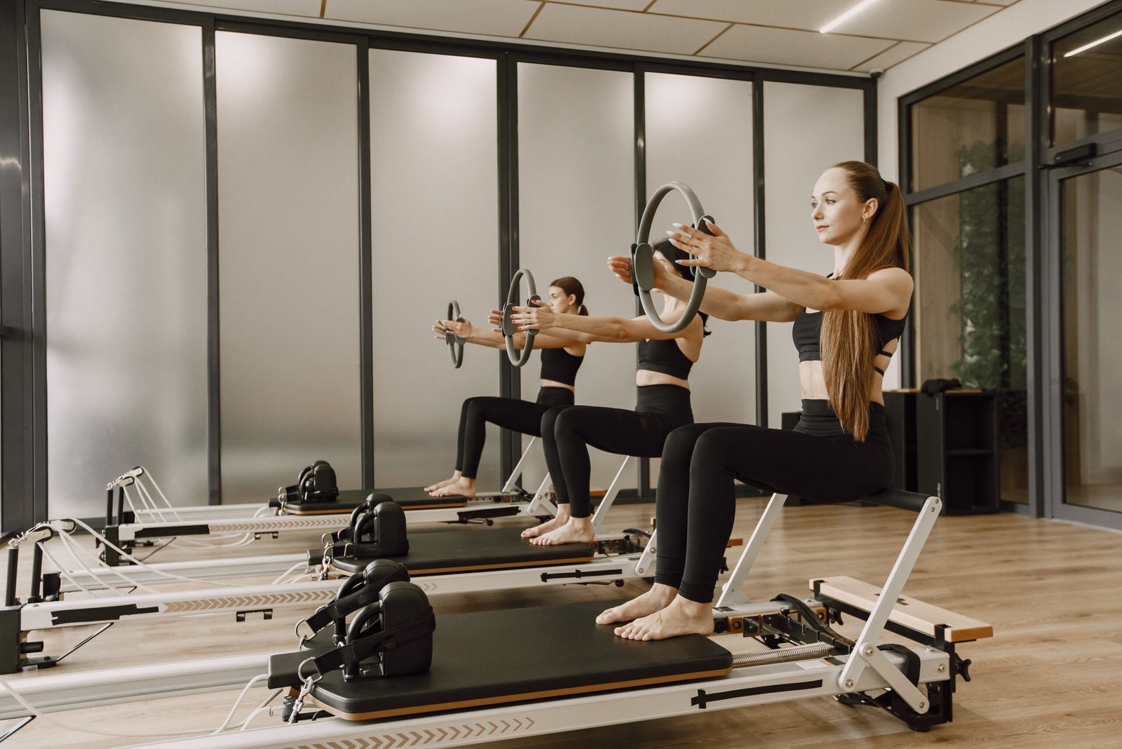 Three young fit women training in gym. Women wearing black sportwears. Caucasian girls excercising with equipment.
