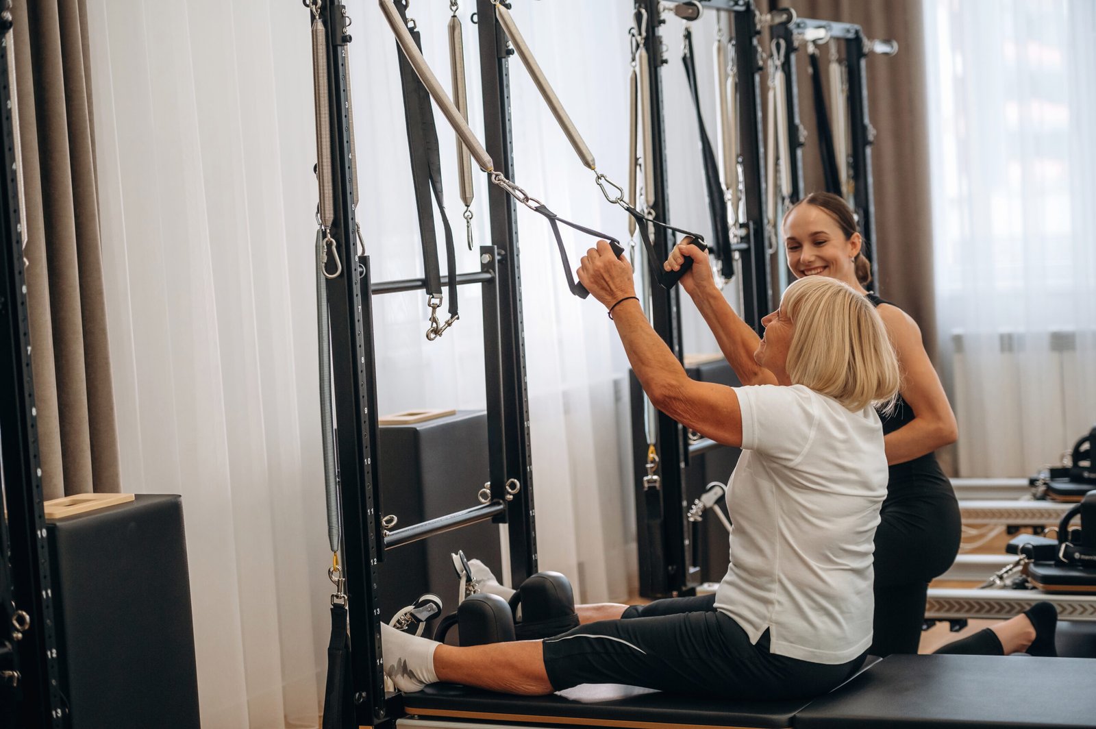 Using training equipment. Female trainer is helping old woman to exercise.