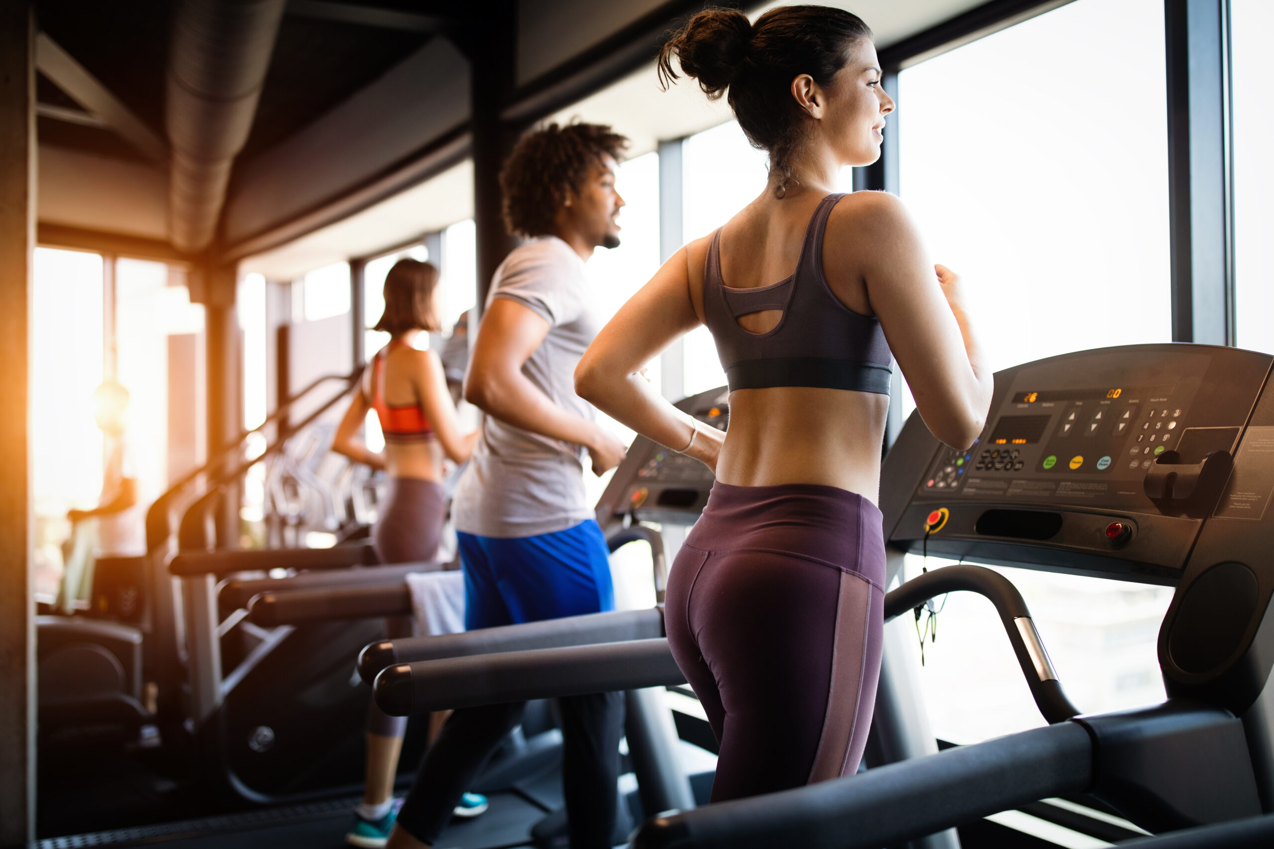 Young fit people running on a treadmill in health club.